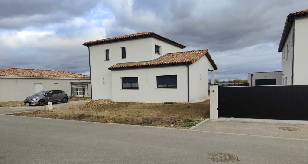 Maison neuve moderne : façade blanche et toit en tuiles Maison neuve contemporaine à façade blanche avec toit en tuiles et volets noirs. Grand portail coulissant noir. Terrain non aménagé.