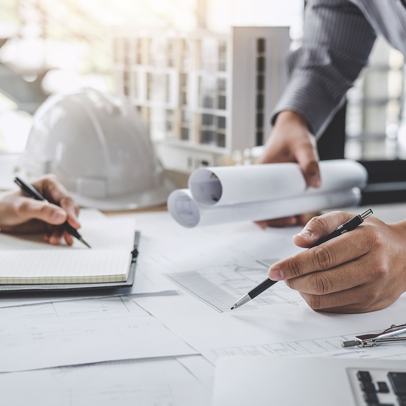 Architecture et construction : Collaboration sur les plans de projet Architectes ou ingénieurs en pleine collaboration sur des plans de construction, avec prise de notes, casque de sécurité et maquette.