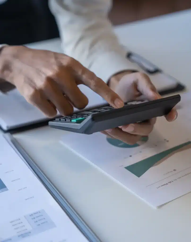 Calculs financiers précis : analyse de données et comptabilité. Mains utilisant une calculatrice pour des calculs financiers. Documents de comptabilité, graphiques d'analyse de données et montants (ex. 37 500 $) sur un bureau.