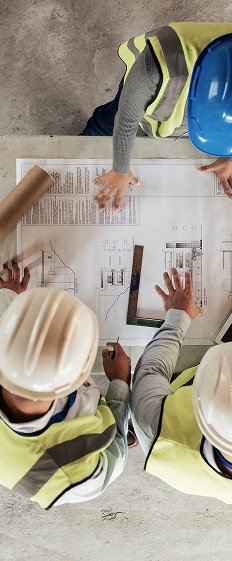 Plans de construction: réunion d'équipe sur le chantier. Quatre professionnels de la construction en gilets et casques de sécurité examinent un plan architectural lors d'une réunion de chantier.